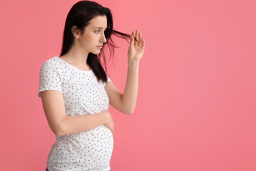 Zwangere vrouw met haaruitval tijdens zwangerschap, die bezorgd naar haar haar kijkt
